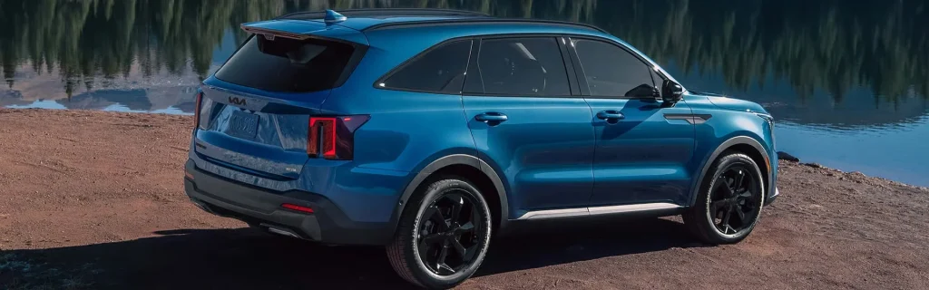 A blue Kia Sorento Hybrid parked by a lake with a scenic backdrop.