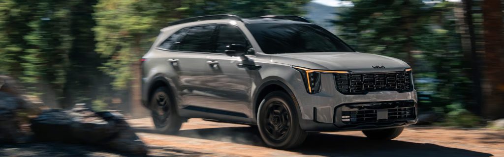 Kia Sorento SUV driving through a wooded road in motion.
