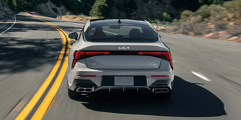 Gray Kia K5 driving along a winding two-lane road.